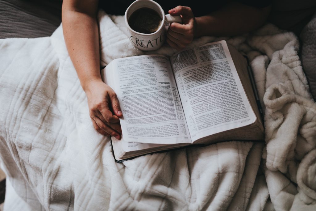 cozy woman under a blanket with her open bible and a cup of coffee