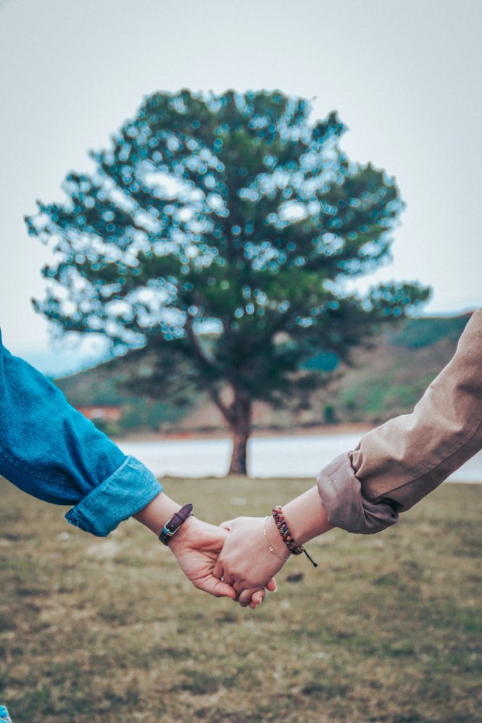 hands of man and woman holding hands in front of a tree