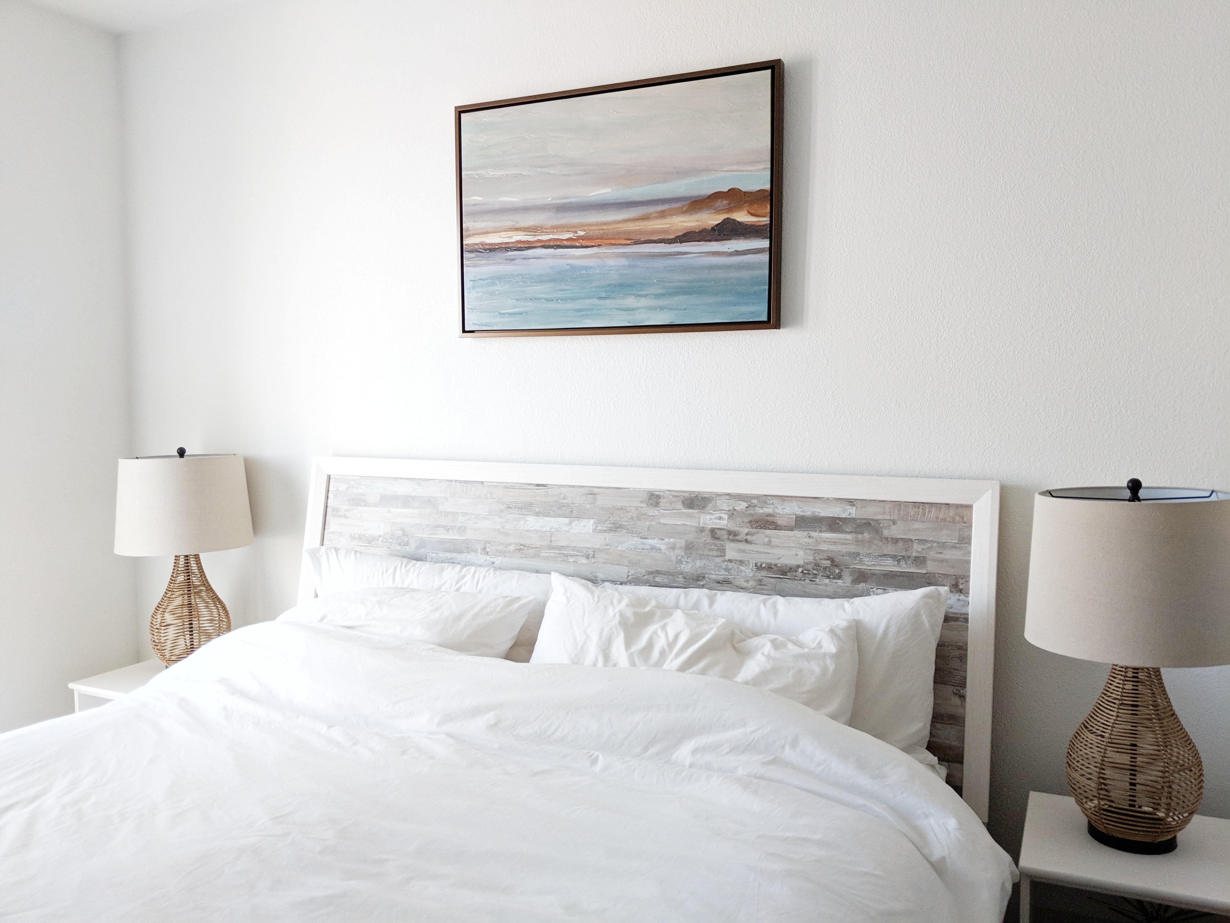 minimalist bedroom with abstract beach painting over the white bed