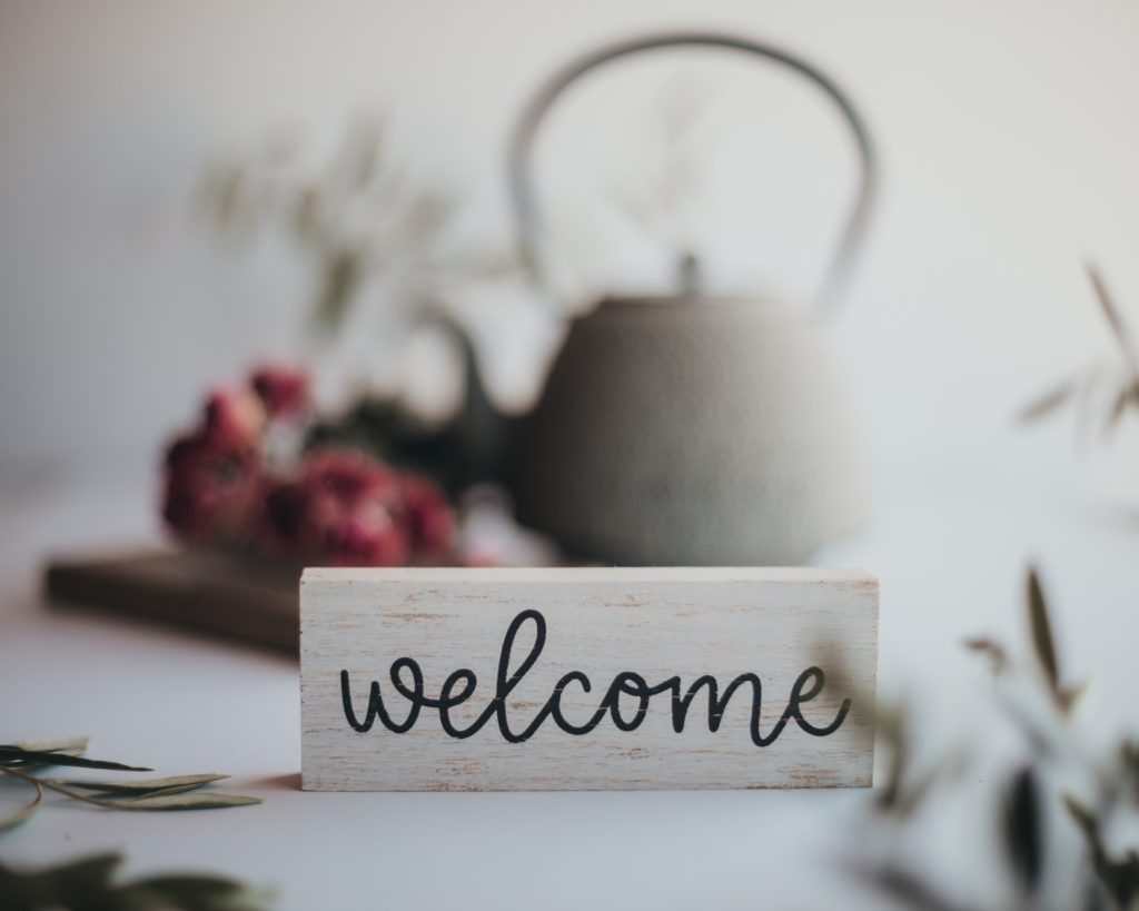 welcome sign in focus with a teapot and flowers blurred behind