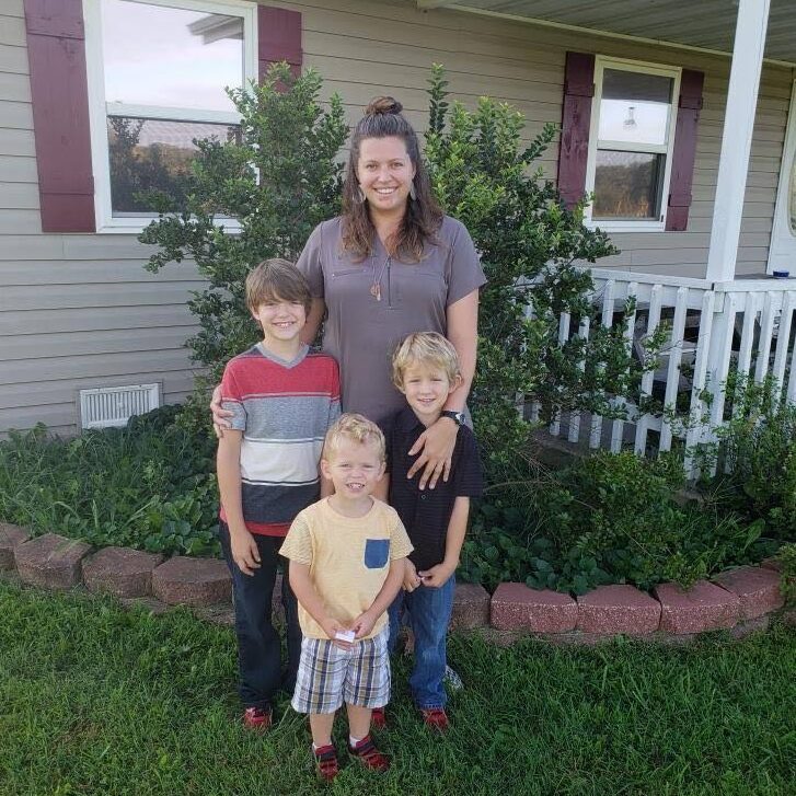 woman and three kids posed in front of house