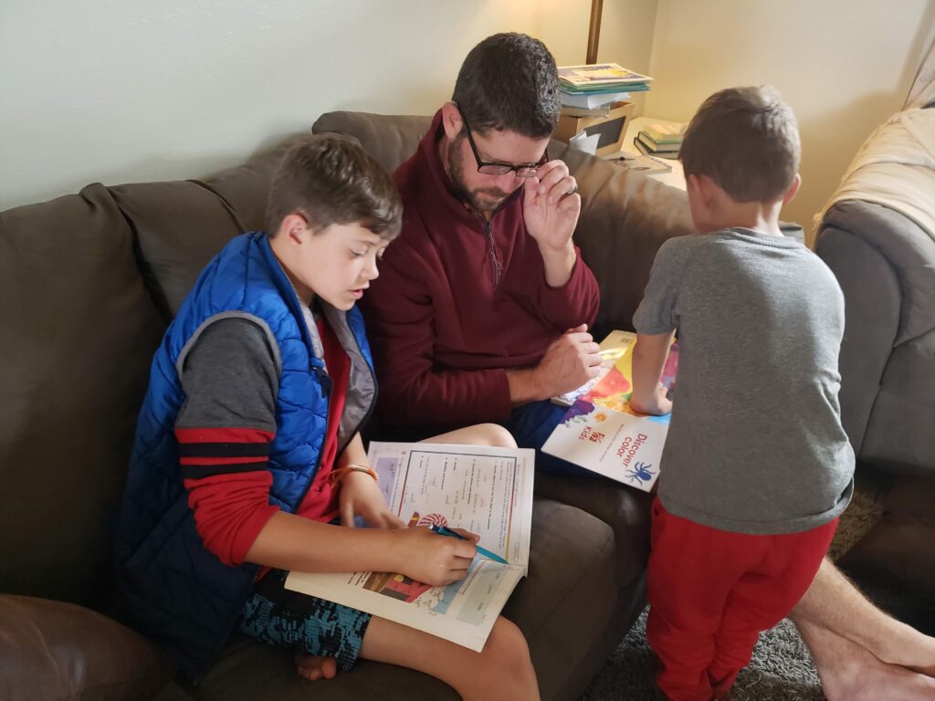 dad on the couch teaching math to one child and hearing a story from another young boy