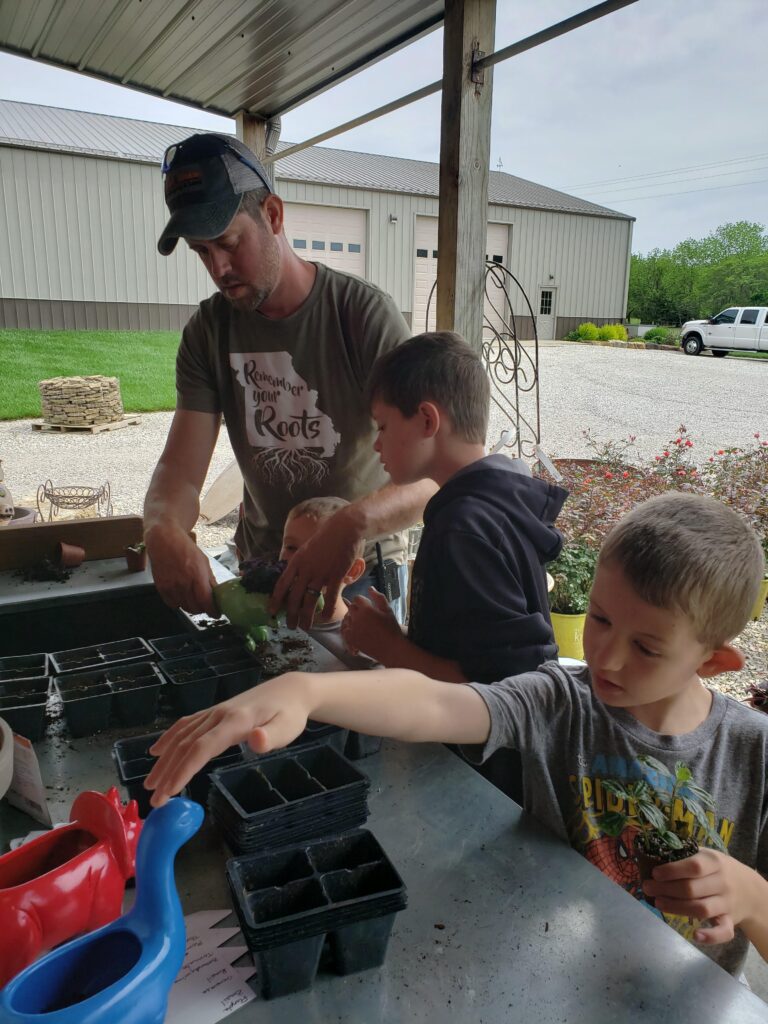 man with two young boys potting plants on an outdoor potting bench