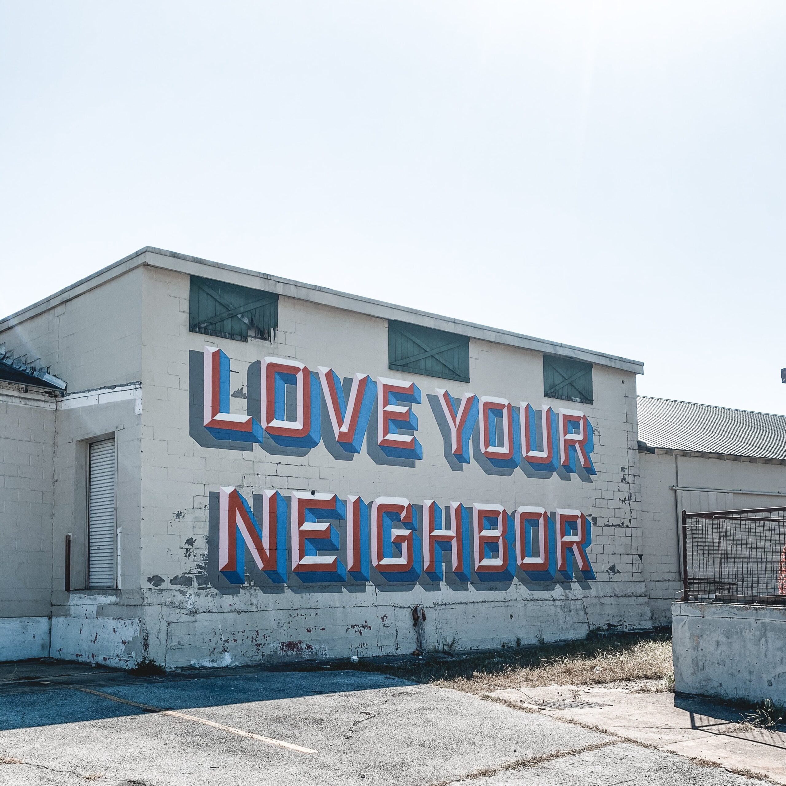 old white brick building with Love Your Neighbor painted as a mural