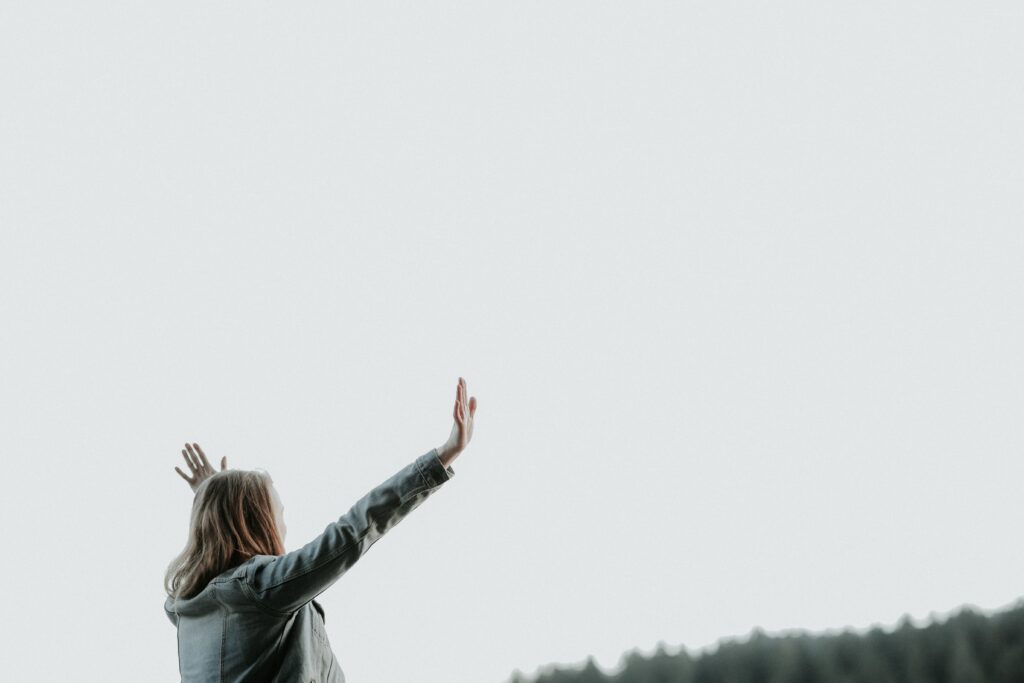 woman outside facing away with arms up toward the sky