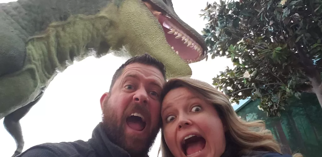 silly selfie of husband and wife under a dinosaur in a museum