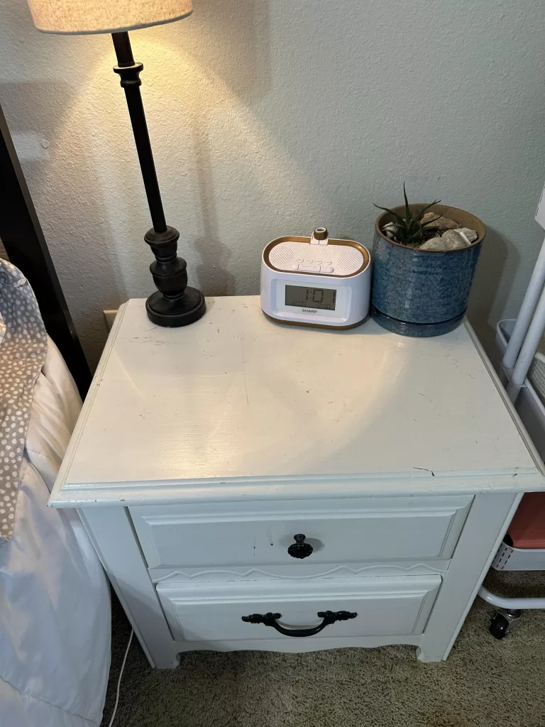 white bedside table with alarm clock, lamp, and small plant