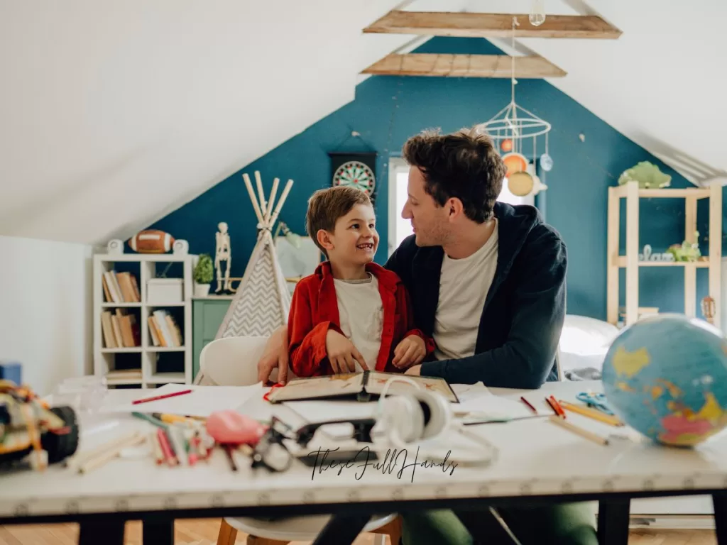 father and son working on homeschool lesson at a table with various materials and supplies on top