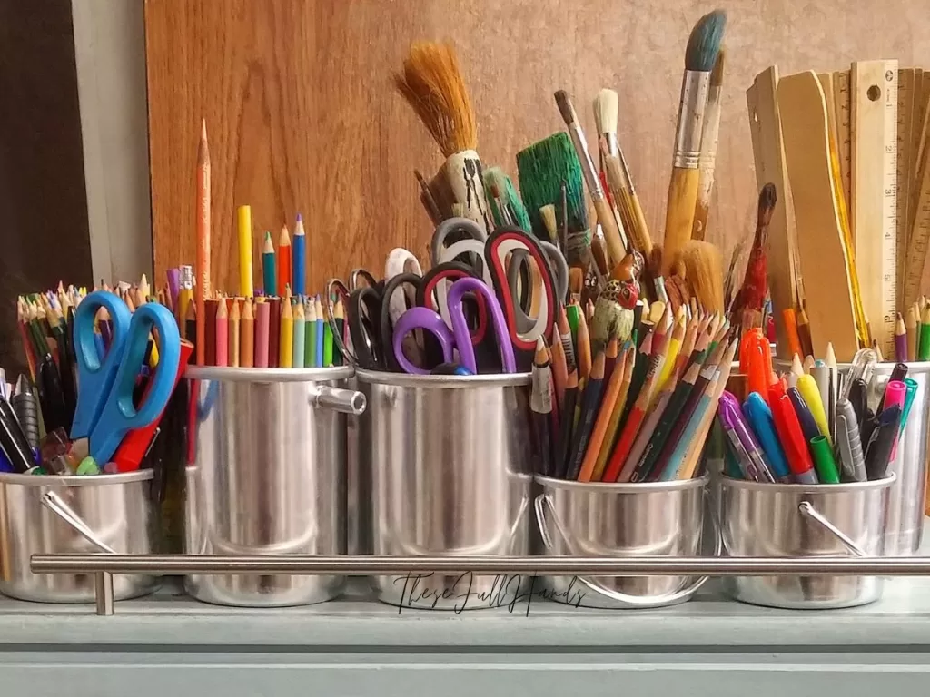 aluminum cups filled with scissors, pencils, paintbrushes, markers, and rulers