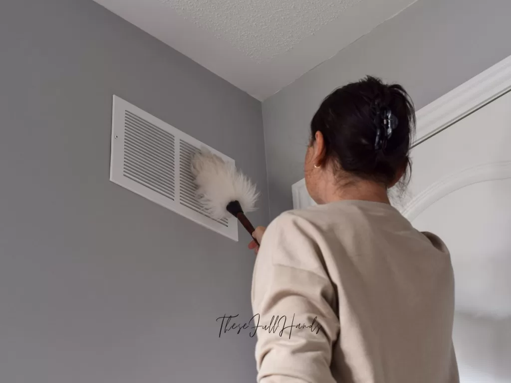 woman dusting the register vent in her wall by the door