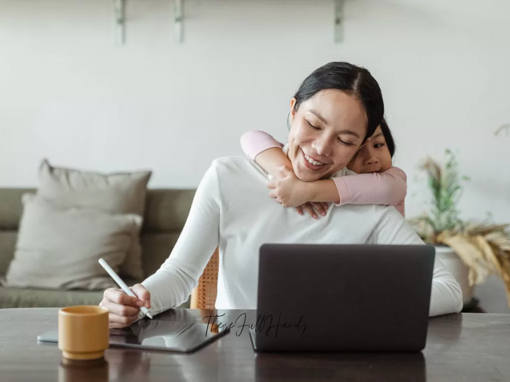 homemaker working on the computer and receiving a hug from her daughter