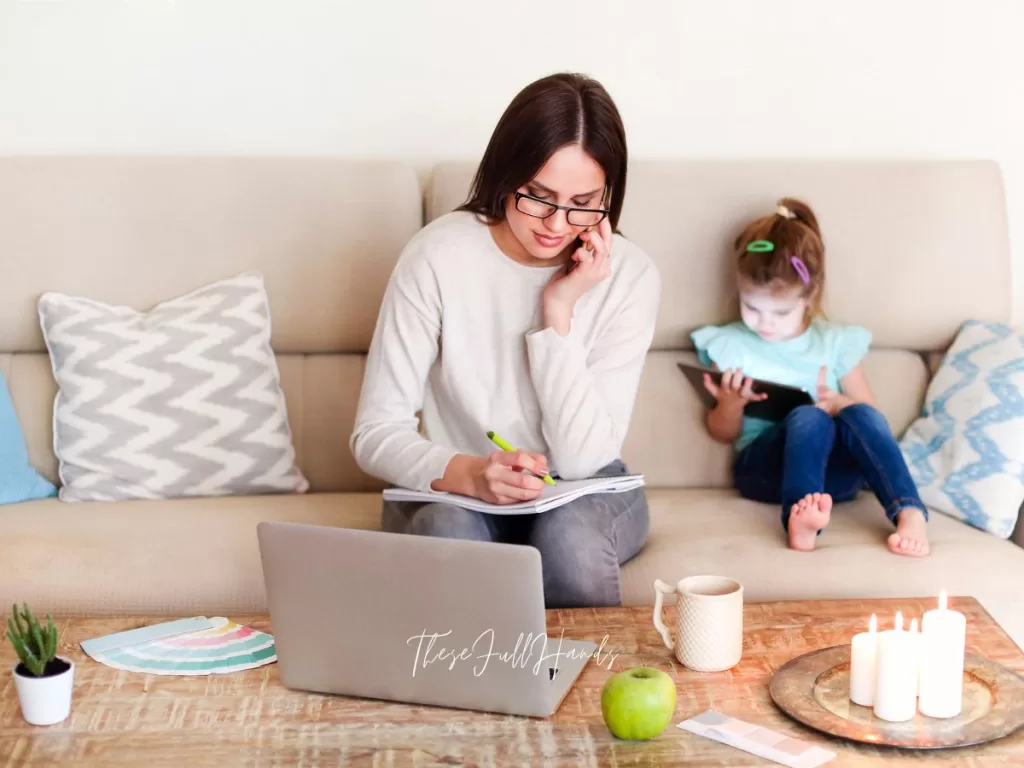 Homemaker managing on the computer with her daughter on the couch behind her