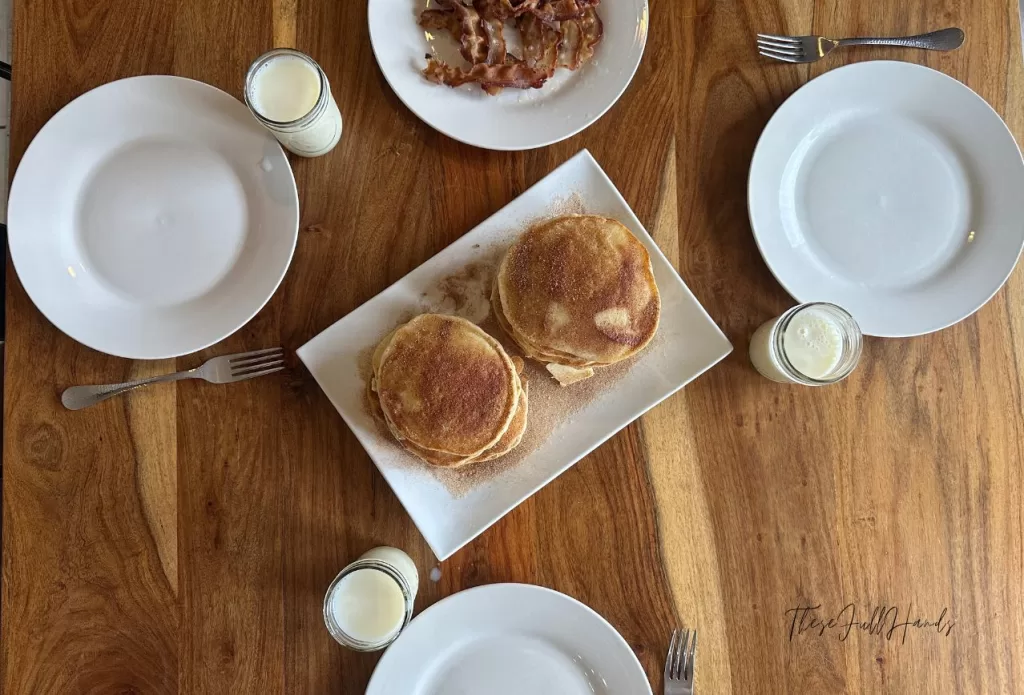 snickerdoodle sourdough discard pancakes set on a plate at the breakfast table with a side of bacon. 