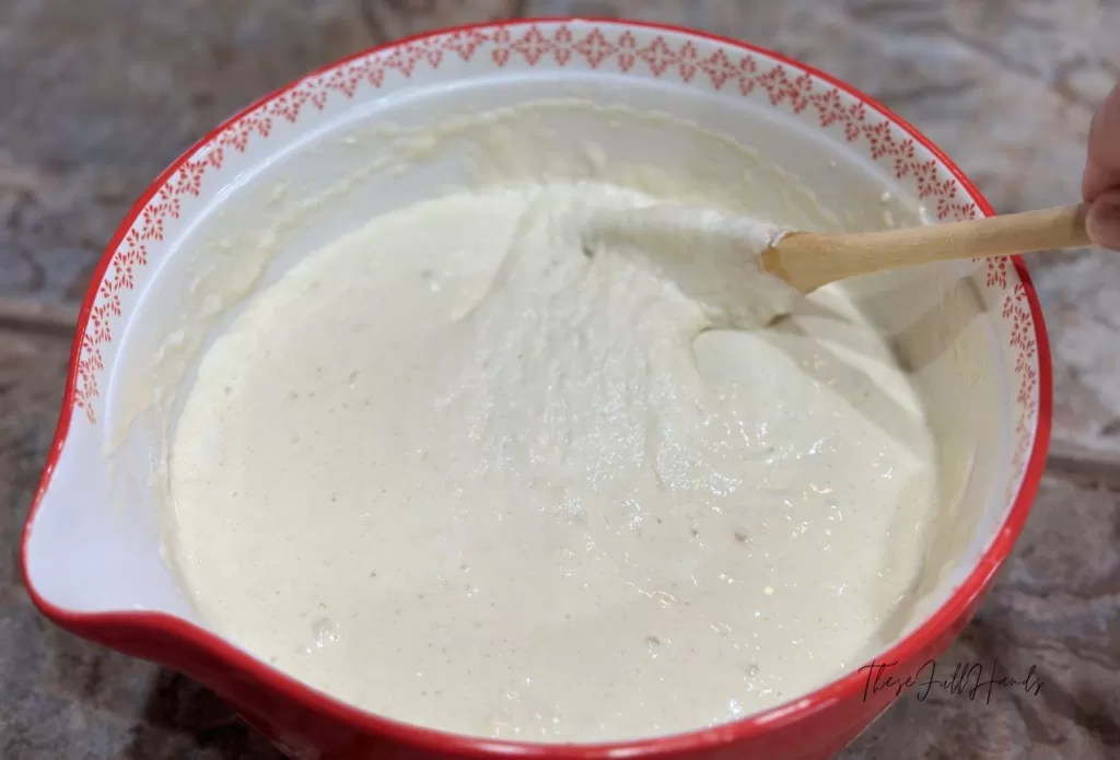 finished pancake batter in a red and white mixing bowl stirred with a wooden spoon