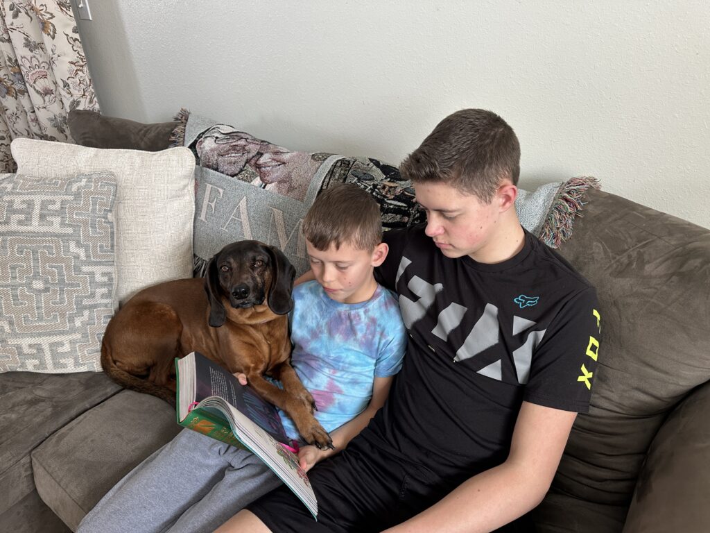 two boys reading bible on the couch with dog