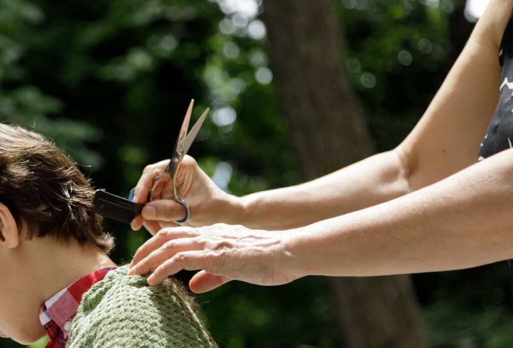 girl's hands cutting boy's hair outside as a money saving tip for single income families