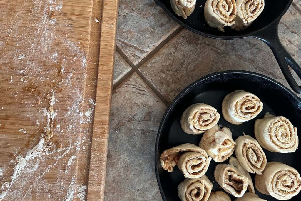 cinnamon roll segments arranged in cast iron skillets ready to bake