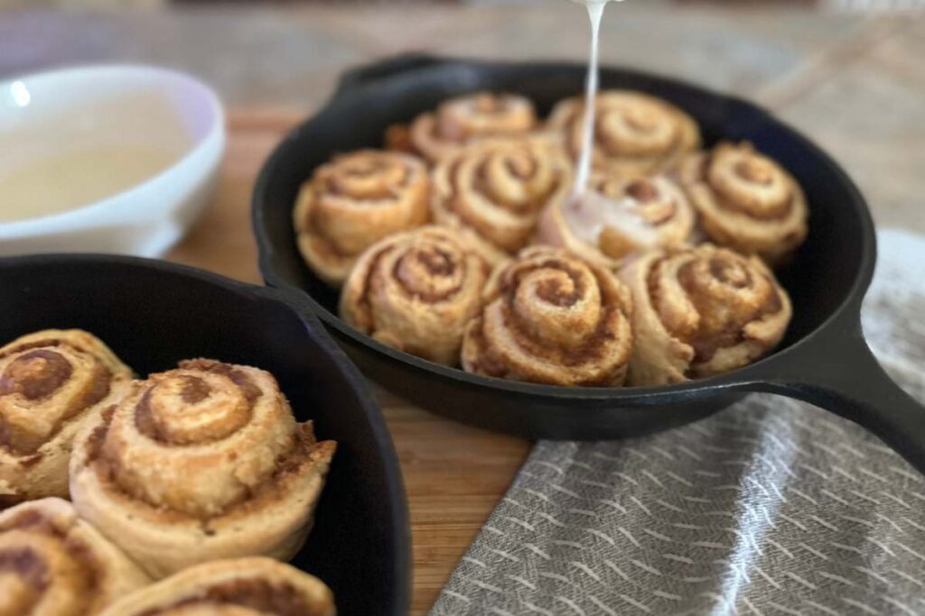 drizzle of glaze being poured over baked cinnamon rolls