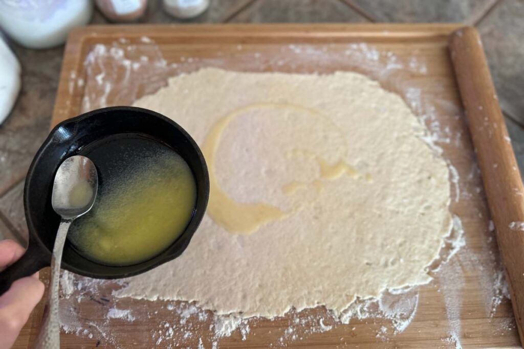 hand spreading melted butter over rolled out cinnamon roll pastry