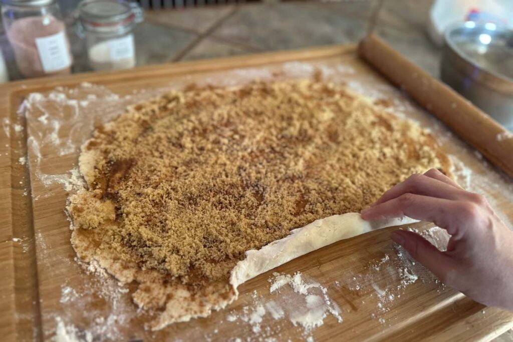 hand rolling up dough covered in cinnamon and sugar