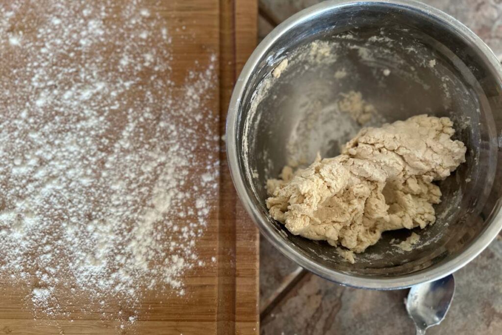 mixed pastry dough in a mixing bowl next to a floured cutting board