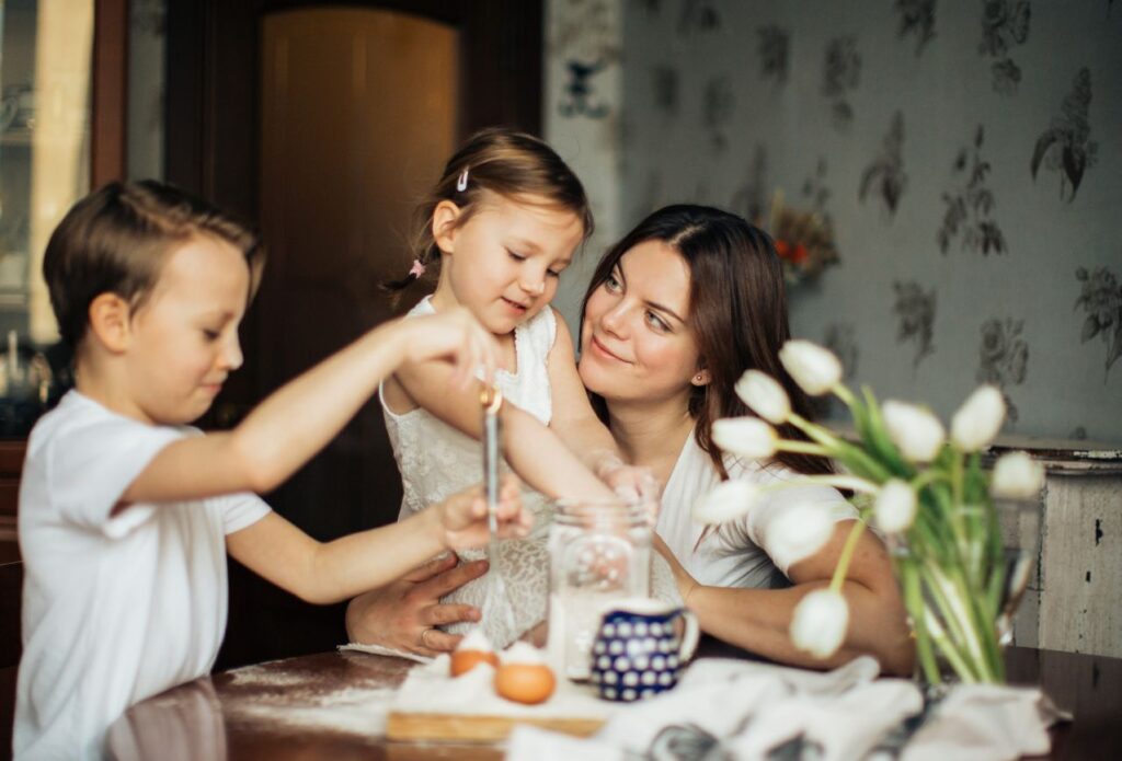 mom homemaker smiling at her young children while they are helping her bake in the kitchen