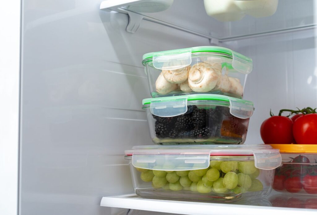 glass rectangular containers in the fridge filled with grapes, berries, and mushrooms